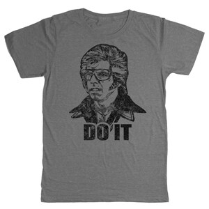 以下が含まれることがあります： メガネをかけた男性の白黒グラフィックが特徴のグレーのTシャツ。「DO IT」の文字が画像の下に黒で印刷されています。シャツは柔らかい素材でできており、半袖です。