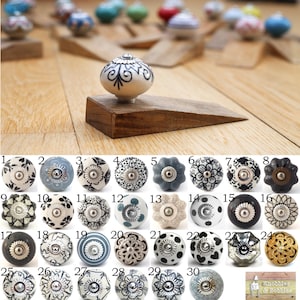 May include: A selection of decorative ceramic knobs in diverse designs and colours, including floral, geometric, and abstract patterns. The knobs are displayed on wooden doorstops. The image also includes the text "Knobblas & Bobblas".