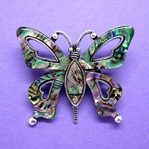 May include: A silver butterfly brooch with iridescent green, blue, and purple abalone shell wings.