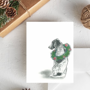 May include: A black and white dog wearing a green Christmas wreath with red ornaments. The dog is sitting and looking to the left.