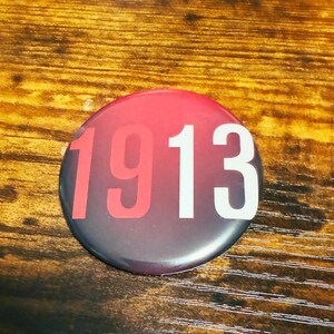 May include: A red, white, and black button with the number 1913 printed on it.
