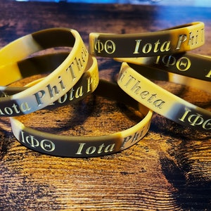 May include: Five brown and tan rubber bracelets with the text "Iota Phi Theta" and the Greek letters "IΦΘ" in gold lettering.
