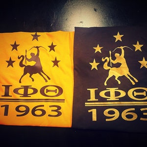 May include: Two t-shirts, one yellow and one black, with a gold design. The design features a centaur-like figure with a bow and arrow, surrounded by stars. The text "IPΘ 1963" is printed below the design.