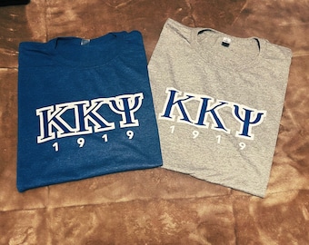 Könnte beinhalten: Zwei T-Shirts, eines blau und eines grau, mit den Buchstaben "KKΨ" und den Zahlen "1919" bedruckt.