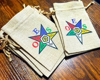 May include: A stack of small, beige burlap bags with a drawstring closure. Each bag features a colorful five-pointed star with the letters "O.E.S." and a Masonic symbol in the center.