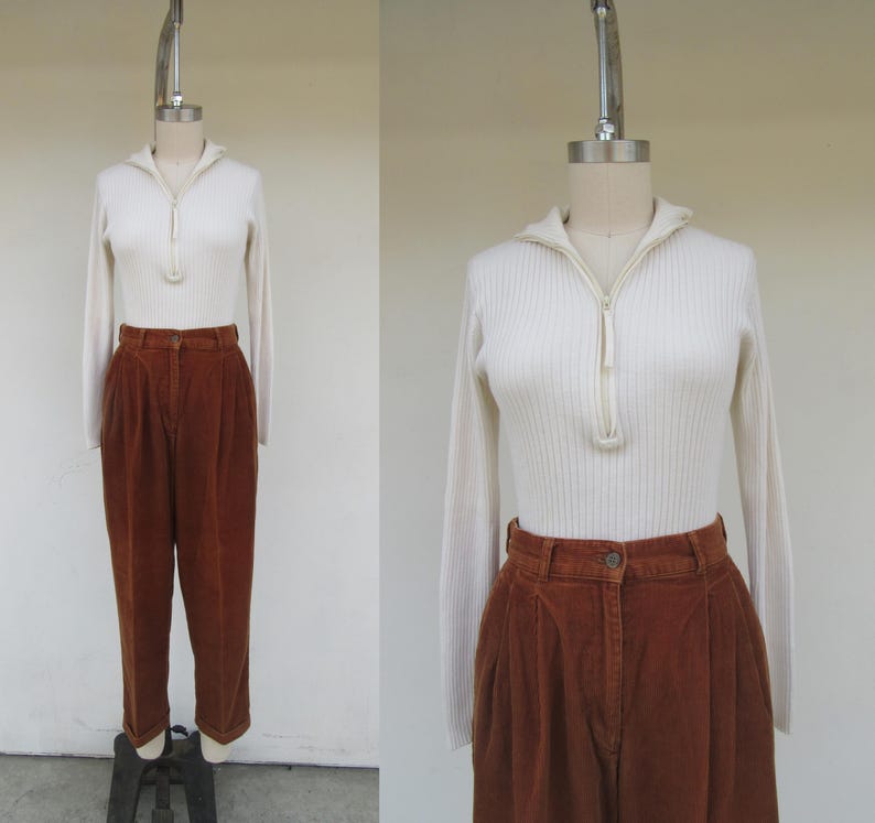 May include: A white ribbed sweater with a zipper neckline and long sleeves. The sweater is paired with brown corduroy pants with pleats.