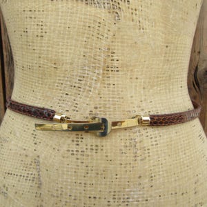 May include: A brown leather belt with a gold buckle. The belt is on a mannequin.