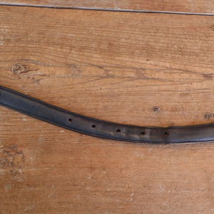 May include: A black leather belt with a decorative silver buckle. The belt has several holes for adjustment and shows signs of wear. The background is a wooden surface.