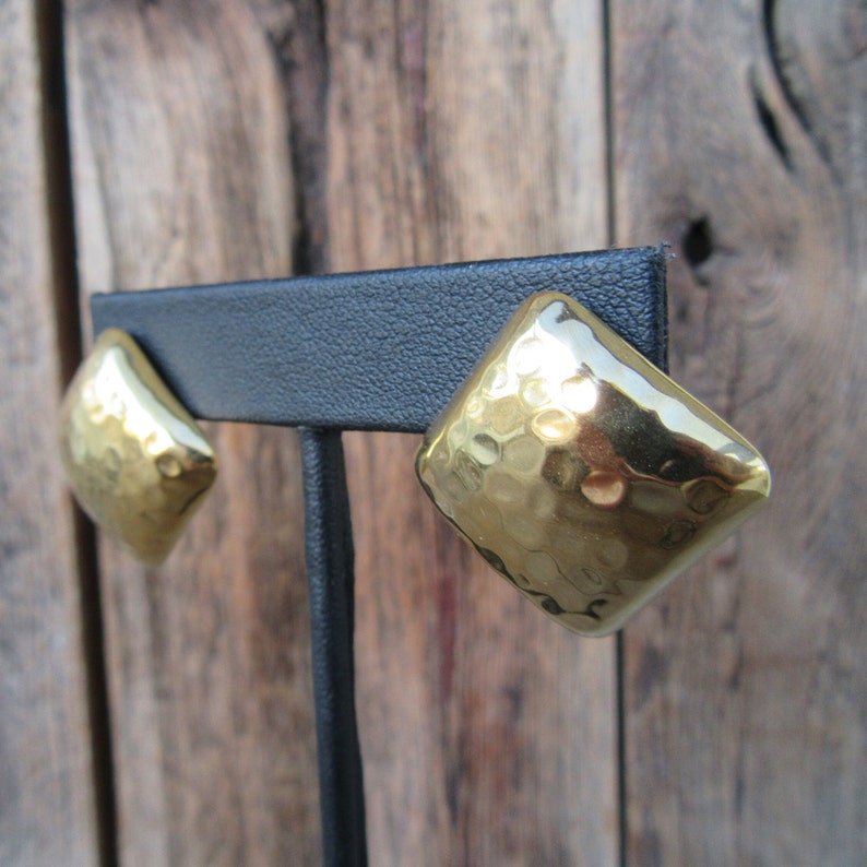 May include: A pair of gold-toned square-shaped earrings with a hammered texture.