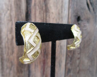 May include: A pair of gold hoop earrings with a white geometric pattern. The earrings are on a black display stand.