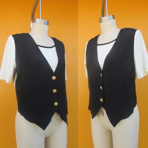Peut inclure: Un gilet sans manches noir avec des boutons dor&eacute;s. Le gilet a une ourlet pointu et est port&eacute; sur une chemise blanche.