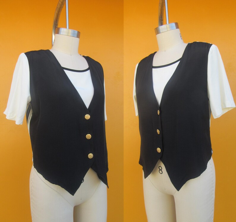 Peut inclure: Un gilet sans manches noir avec des boutons dor&eacute;s. Le gilet a une ourlet pointu et est port&eacute; sur une chemise blanche.