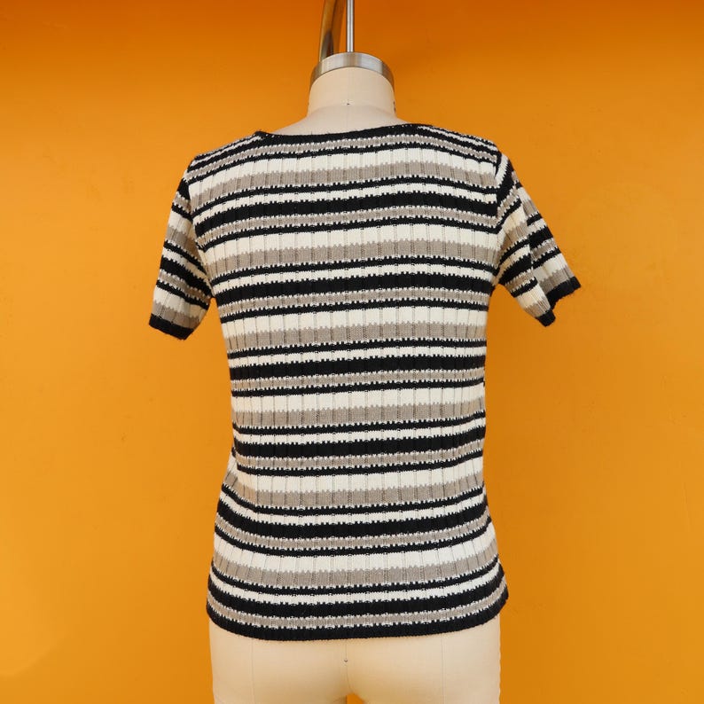 May include: A striped short-sleeved shirt with black, white and grey horizontal stripes. The shirt is made of a ribbed knit fabric.