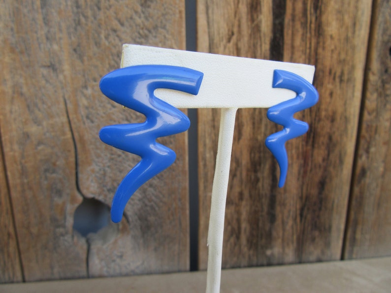 May include: A pair of blue abstract shaped earrings. The earrings are made of plastic and have a glossy finish.