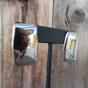 May include: A pair of silver earrings with a rectangular shape. The earrings are on a black display stand.