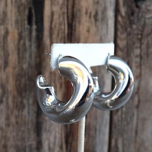 May include: A pair of silver hoop earrings with a twisted design. The earrings are made of metal and have a shiny finish.