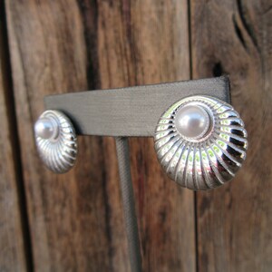 May include: A pair of silver tone earrings with a faux pearl centre. The earrings have a scalloped design.