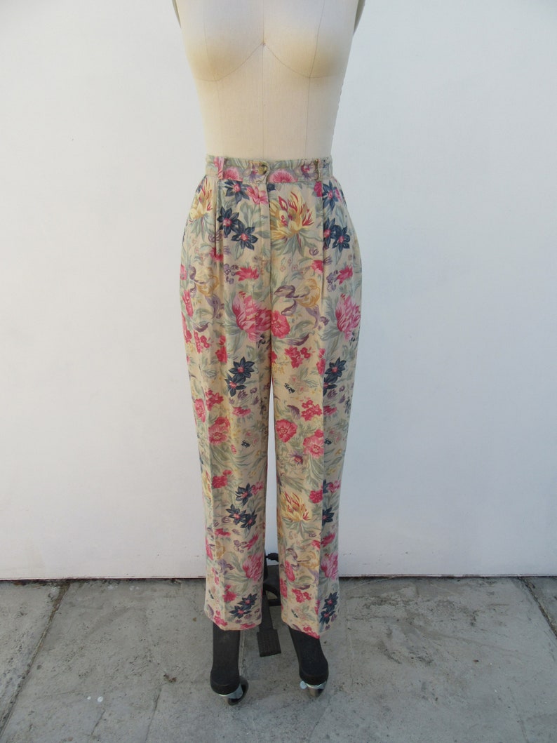 May include: High-waisted pants with a floral print in shades of pink, yellow, green, and blue. The pants have a pleated front and a straight leg.