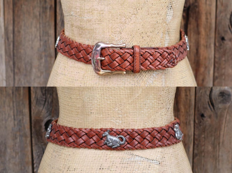 May include: A brown leather belt with a woven design. The belt has a silver buckle and decorative silver accents. The belt is displayed on a mannequin. The belt is approximately 3.8 cm wide.
