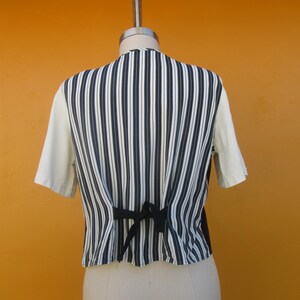 Peut inclure: Un gilet &agrave; rayures blanches et noires avec un n&oelig;ud de ruban noir dans le dos. Le gilet est sur un mannequin blanc.