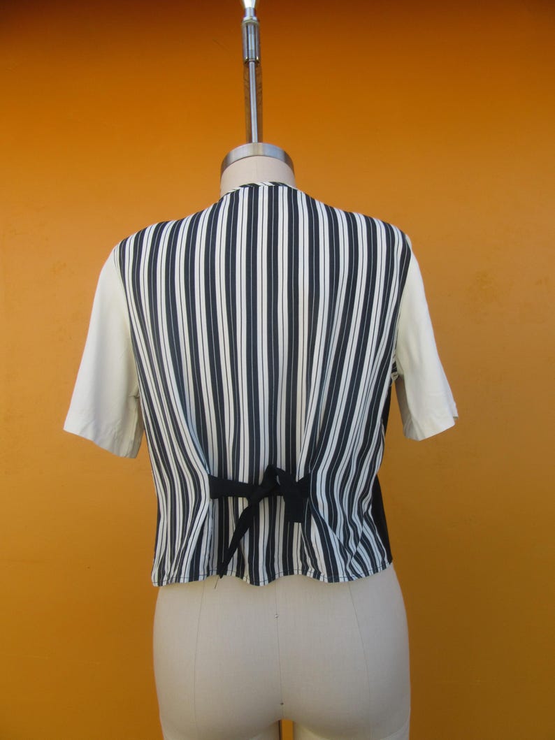 Peut inclure: Un gilet &agrave; rayures blanches et noires avec un n&oelig;ud de ruban noir dans le dos. Le gilet est sur un mannequin blanc.