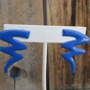 May include: A pair of blue abstract shaped earrings. The earrings are made of a smooth, glossy material and have a wavy, organic design.