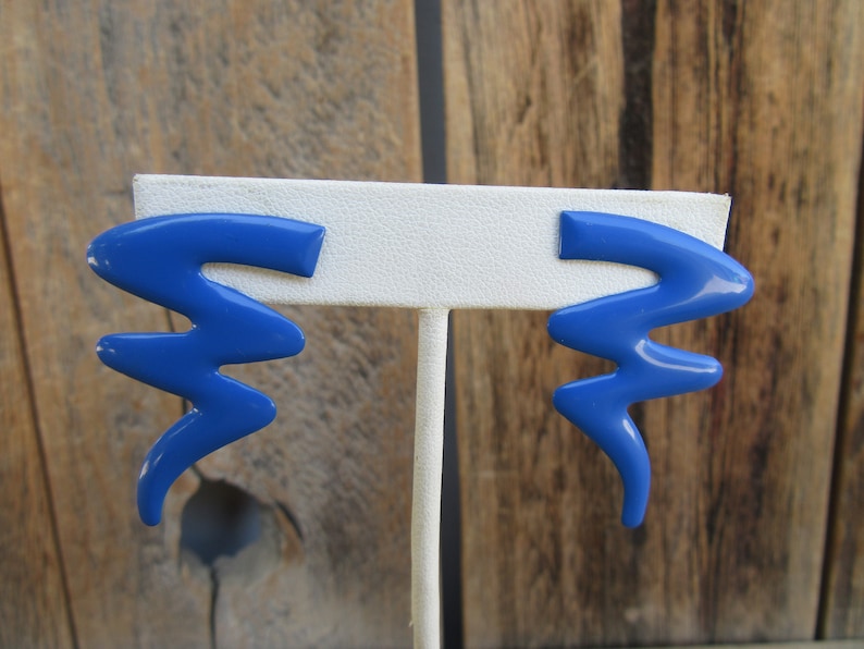 May include: A pair of blue abstract shaped earrings. The earrings are made of a smooth, glossy material and have a wavy, organic design.