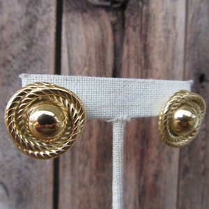 May include: A pair of gold-tone earrings with a rope-like design around the edges. The earrings have a round, slightly domed center.