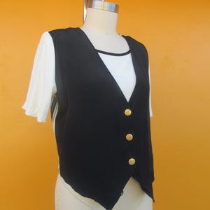 Peut inclure: Un gilet noir sans manches avec des boutons dor&eacute;s. Le gilet a un col en V et est fait d'un tissu soyeux.
