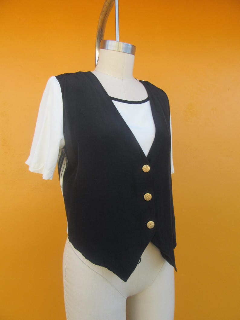 Peut inclure: Un gilet noir sans manches avec des boutons dor&eacute;s. Le gilet a un col en V et est fait d'un tissu soyeux.