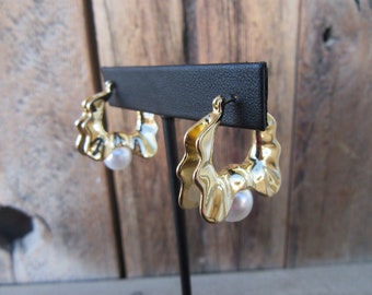 May include: Gold hoop earrings with a textured, wavy design and a single pearl accent on each earring.