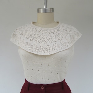 Puede incluir: Un top blanco de crochet con un amplio cuello festoneado y sin mangas. El top se combina con una falda color burdeos.