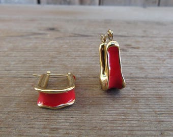 May include: A pair of gold hoop earrings with red enamel. The earrings are simple and elegant.