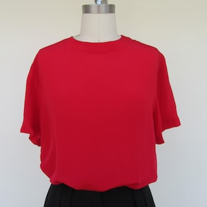 May include: A red short-sleeved blouse with a round neckline. The blouse is on a mannequin and is paired with a black skirt.