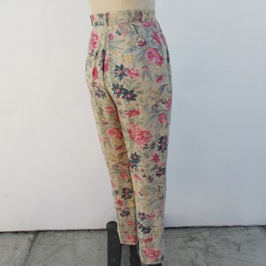 May include: High-waisted pants with a floral print in shades of pink, blue, and green on a beige background.