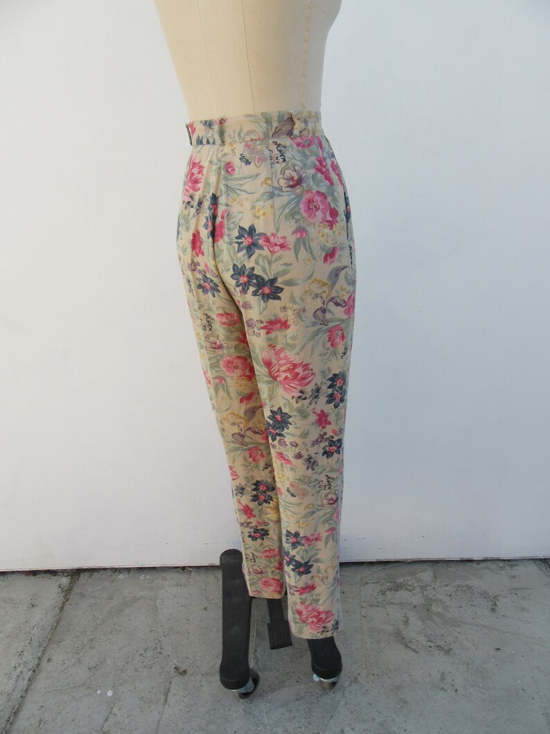 May include: High-waisted pants with a floral print in shades of pink, blue, and green on a beige background.