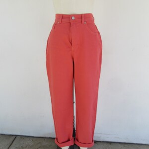 May include: Coral-colored high-waisted jeans with a button closure and classic five-pocket design. The jeans have a straight leg and are cuffed at the ankles. The pants are displayed on a mannequin.