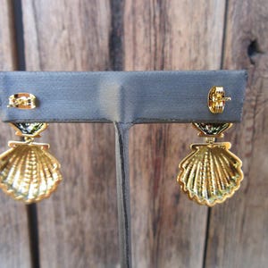 May include: A pair of gold tone earrings with a seashell design. The earrings have a green and black enamel detail.