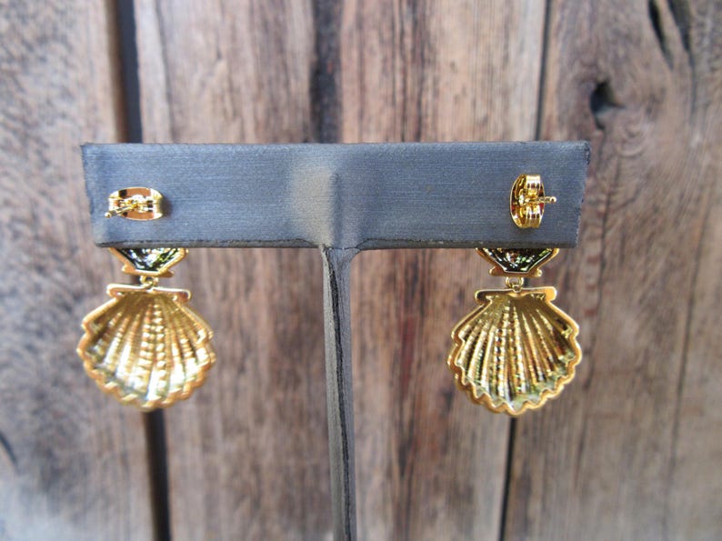 May include: A pair of gold tone earrings with a seashell design. The earrings have a green and black enamel detail.
