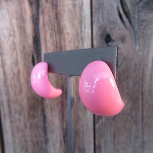 May include: A pair of pink plastic clip-on earrings. The earrings are shaped like a half-circle and have a glossy finish.