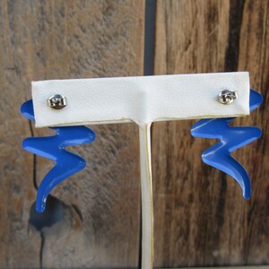May include: A pair of blue lightning bolt shaped earrings with silver posts. The earrings are displayed on a white earring stand.
