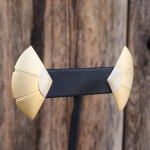 Puede incluir: Un par de pendientes de tono dorado con un diseño en forma de abanico. Los pendientes tienen un centro blanco y se muestran en un soporte negro.
