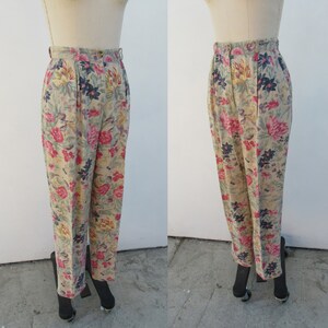 May include: Beige high-waisted pants with a floral print featuring pink, red, blue, and yellow flowers. The pants have a wide leg and a relaxed fit.
