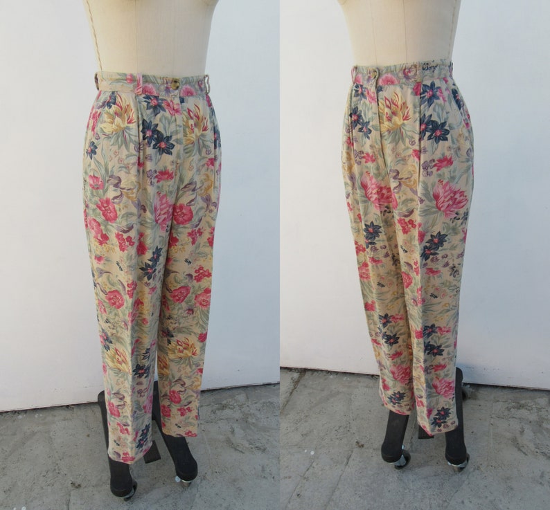 May include: Beige high-waisted pants with a floral print featuring pink, red, blue, and yellow flowers. The pants have a wide leg and a relaxed fit.