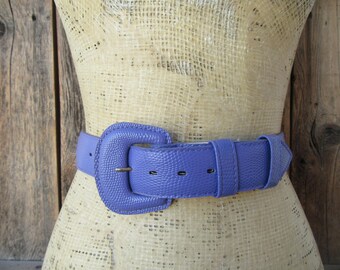 May include: A purple leather belt with a large, rectangular buckle. The belt is made of a textured material and has a smooth finish.