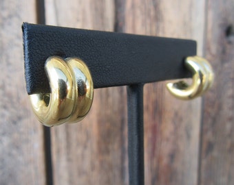 May include: A pair of gold hoop earrings with a twisted design. The earrings are displayed on a black stand.