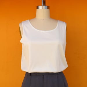 May include: A white sleeveless top with a scoop neck. The top is made of a smooth, silky fabric.