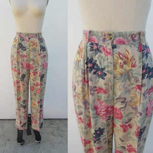 May include: Beige high-waisted pants with a floral print featuring pink, yellow, blue, and green flowers. The pants have a pleated front and a straight leg.