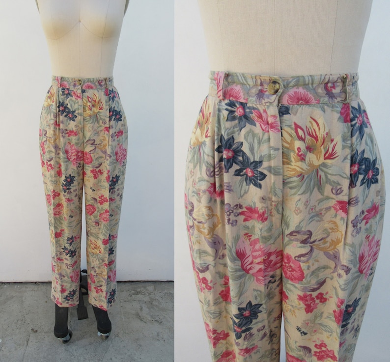 May include: Beige high-waisted pants with a floral print featuring pink, yellow, blue, and green flowers. The pants have a pleated front and a straight leg.