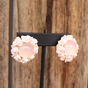 May include: A pair of pink and white floral earrings with a pink cabochon stone in the center of each flower.